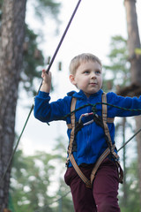 A little boy is training in a rope park. The child climbs the obstacle course. Active recreation in the park in the fresh air.