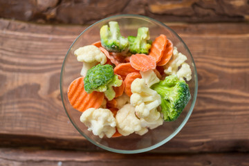 Fresh frozen sliced vegetables - cabbage, carrots in a plate on a wooden background.