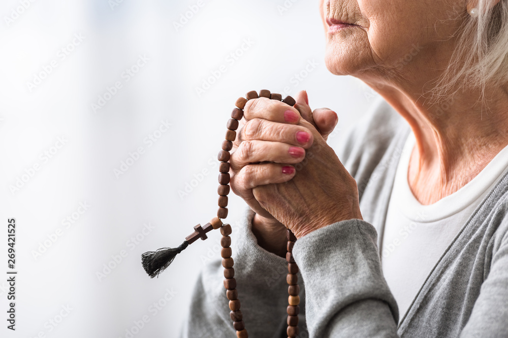 Wall mural partial view of senior woman praying with wooden rosary - Wall murals