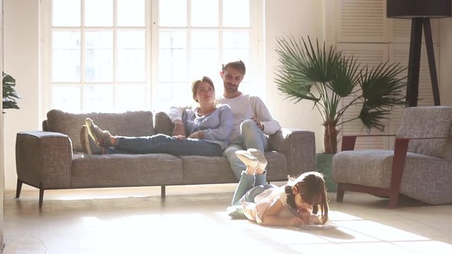 Parents relaxing on sofa while child daughter drawing on floor
