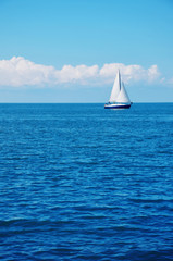 Fototapeta premium Blue sea water and a white sailboat.