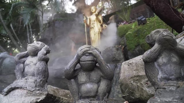hree wise monkeys at golden mount temple Thailand, Bangkok. See no  evil, hear no evil, speak no evil statues in exterior, outside shrine with flowing misty water features.