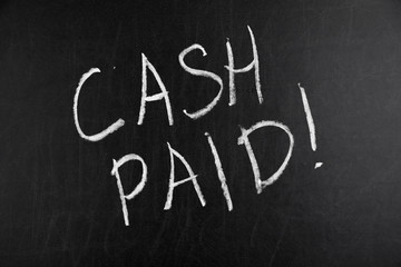 Words Cash Paid written by hand in white chalk on a blackboard