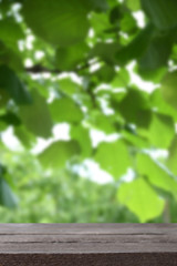  Image of grey wooden table in front of abstract blurred background of green leaves and trees