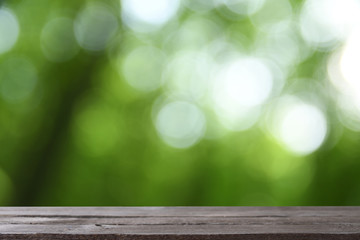  Image of grey wooden table in front of abstract blurred background of green leaves and trees