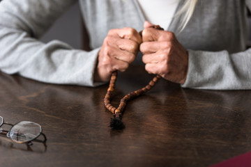 partial view of senior woman holding wooden rosary