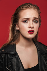 Fototapeta na wymiar Beautiful young sad emotional woman with bright makeup red lipstick posing isolated over red wall background.