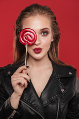 Woman with bright makeup red lipstick posing isolated over red wall background holding candy sweeties.