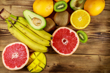 Obraz na płótnie Canvas Assortment of tropical fruits on wooden table. Still life with bananas, mango, oranges, avocado, grapefruit and kiwi fruits