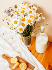 Simply stylish wooden kitchen with bottle of milk and glass on table, summer flowers camomile, healthy foog moring concept close up