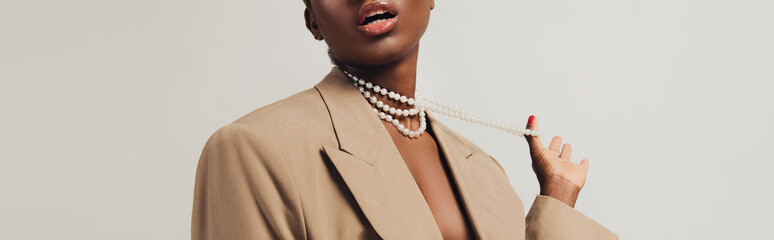 cropped view of seductive african american woman in beige jacket and necklace isolated on grey - obrazy, fototapety, plakaty