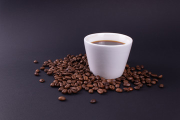 On a dark background a white mug of strong coffee in coffee beans