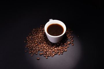 Coffee grains among which there is a cup illuminated by a limited beam from the top