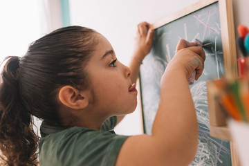 little girl draws concentrated on the chalkboard