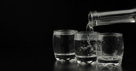 Pouring up shots of vodka from a bottle into glass against black background