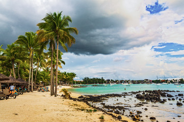 view of the sea beach on a Sunny summer day with palm trees on the shore and black stones
