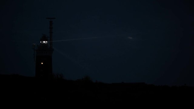 Shining lighthouse on the coast of the island in the evening. The light beam is well visible. No people.