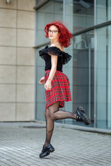 Teen girl bounces on the street. Red hair. Concept of lifestyle, urban, travel, fashion