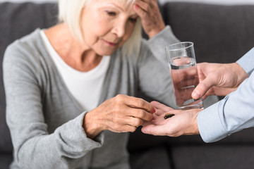 cropped view of man giving to senior mother glass of water and medicine