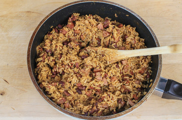 Skillet filled with red beans and rice and chunks of sausage on wooden cutting board