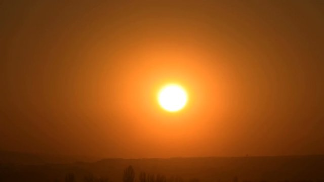 Superzoom plan timelapse sunset with a clear sky in orange tones on a flat horizon