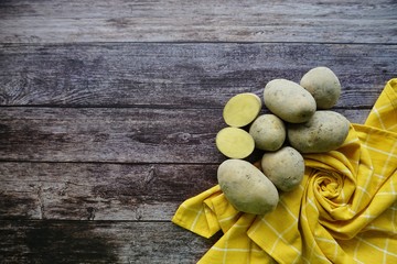 Fresh Potatoes on a yellow weathered cloth over a wooden background, top view
