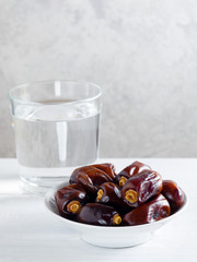 Dry dates and a glass of water on white background. Ramadan, Iftar concept. Vertical orientation, copy space.