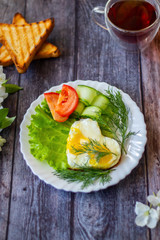 Fried eggs with lettuce, cucumber and tomato slices on wooden background