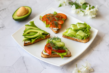 Vegetarian sandwiches with avocado, tomatoes and cucumbers on a light background
