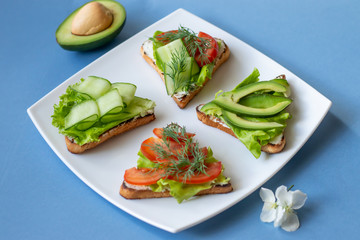 Vegetarian sandwiches with avocado, tomatoes and cucumbers on a blue background