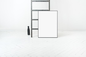 Pusta ramka na plakat oparta o drabinę w minimalistycznie białym pokoju. © Tomasz