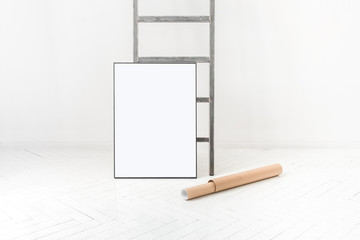 Pusta ramka na plakat oparta o drabinę w minimalistycznie białym pokoju. Tuba na plakat położona na ziemi. © Tomasz