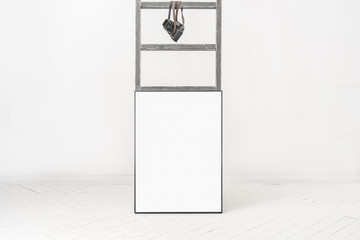 Pusta ramka na plakat oparta o drabinę w minimalistycznie białym pokoju.