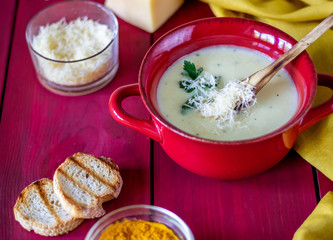 Cheese cream soup on a red wooden background. White bread croutons. Ingredients.