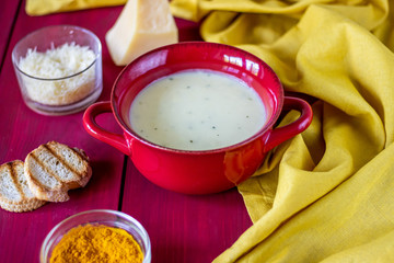 Fototapeta na wymiar Cheese cream soup on a red wooden background. White bread croutons. Ingredients.