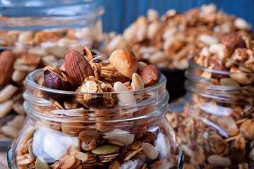 Homemade granola with different nuts and seeds in glass jars against the blue background