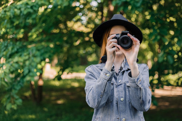 attractive young girl in a hat makes photo on camera outdoors