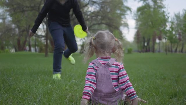 Older brother and small sister run in beautiful green park. Small girl fall down and boy help her to stand up. Happy family.