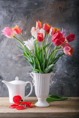 A bouquet of tulips in a vase and a white kettle on the table.