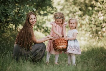 family photo mom with daughters in the park. Photo of young mother with two cute kids outdoors in spring time, beautiful woman with daughter having fun