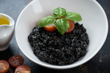 Squid-ink risotto with cherry tomatoes, fresh green basil and olive oil, closeup