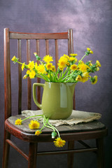 A bouquet of dandelions in a vase on a chair.