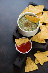 Wooden serving tray with nachos and freshly made guacamole, vertical shot on a brown metal surface