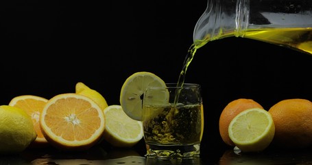 Pour juice from pitcher into glass, orange and lemon slices on background