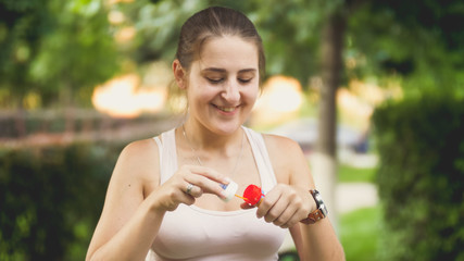 Closeup portrait of beautiful smiling young woman blowing soap bubbles in park at sunset