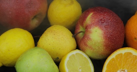 Tropical lemon, orange, apple in cold ice clouds of fog smoke on dark background