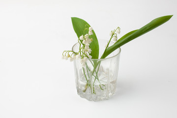 Lily of the valley flowers in a glass on a white background.