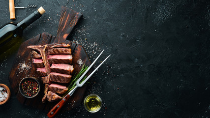Beef T-Bone steak on a black table. Top view. Free space for text. - obrazy, fototapety, plakaty