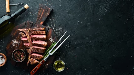 Rolgordijnen Rundvlees T-Bone steak op een zwarte tafel. Bovenaanzicht. Vrije ruimte voor tekst. © Yaruniv-Studio