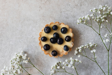 Tartalette with big blackberries with airy flowers on a gray background with copy space.